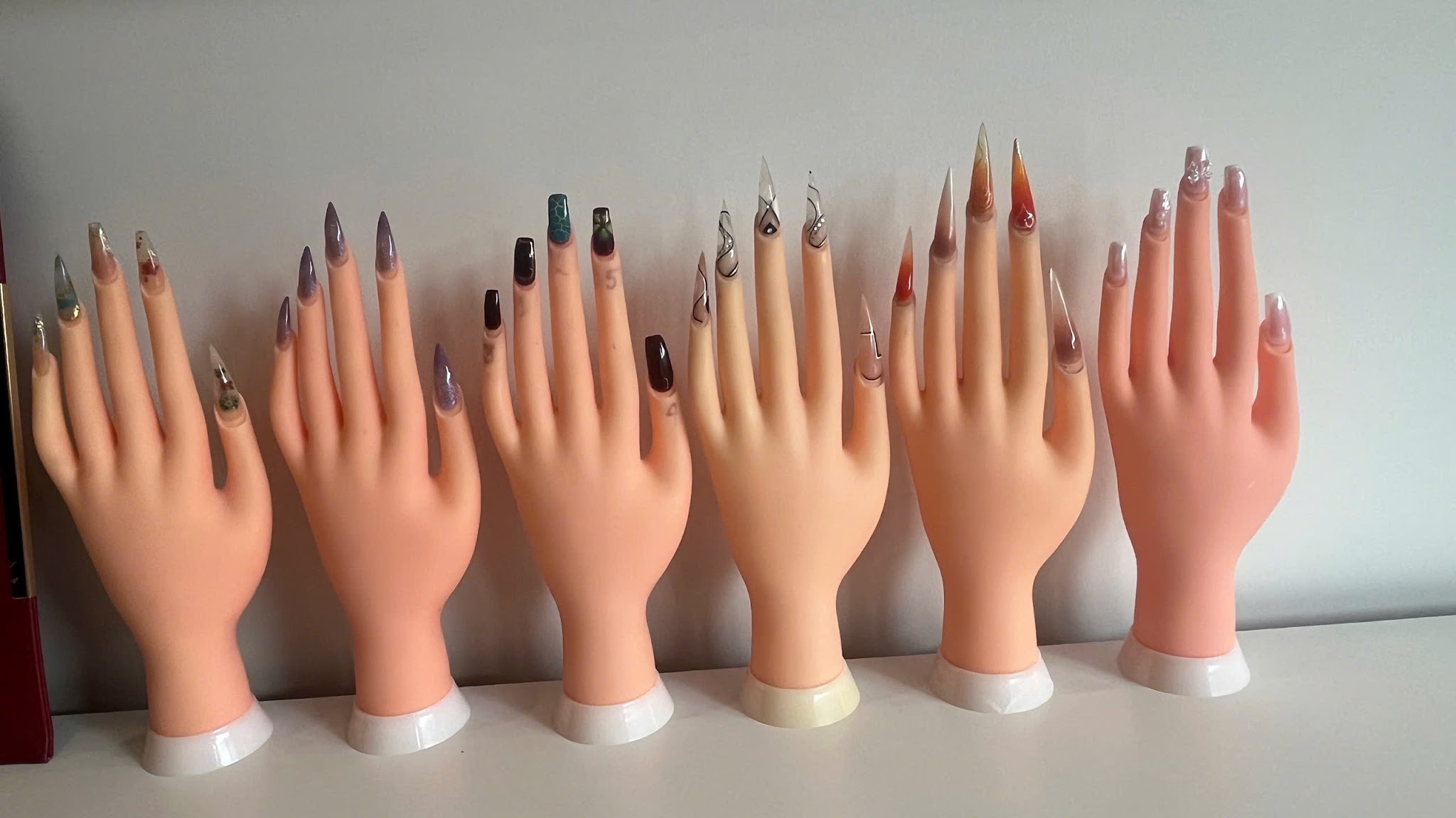 Zes oefenhanden op een rij, elk met lange nagels in een ander ontwerp